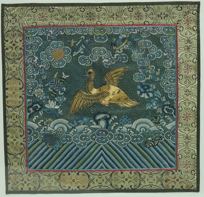 A framed late 19th early 20th century Chinese Mandarin Rank Badge. Worked with a gold thread central motif of a Phoenix, surrounded by finely silk embroidered auspicious motifs, clouds and rolling sea beneath. Bordered w